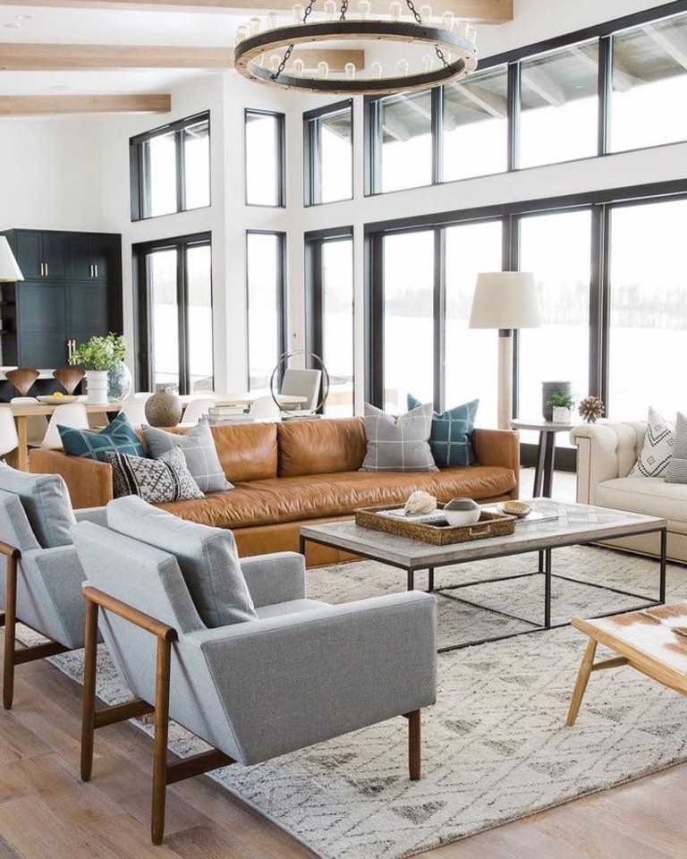 Double-height living room with black-framed windows, white oak ceiling beams, a round wood-and-iron ring chandelier and a cognac leather sofa