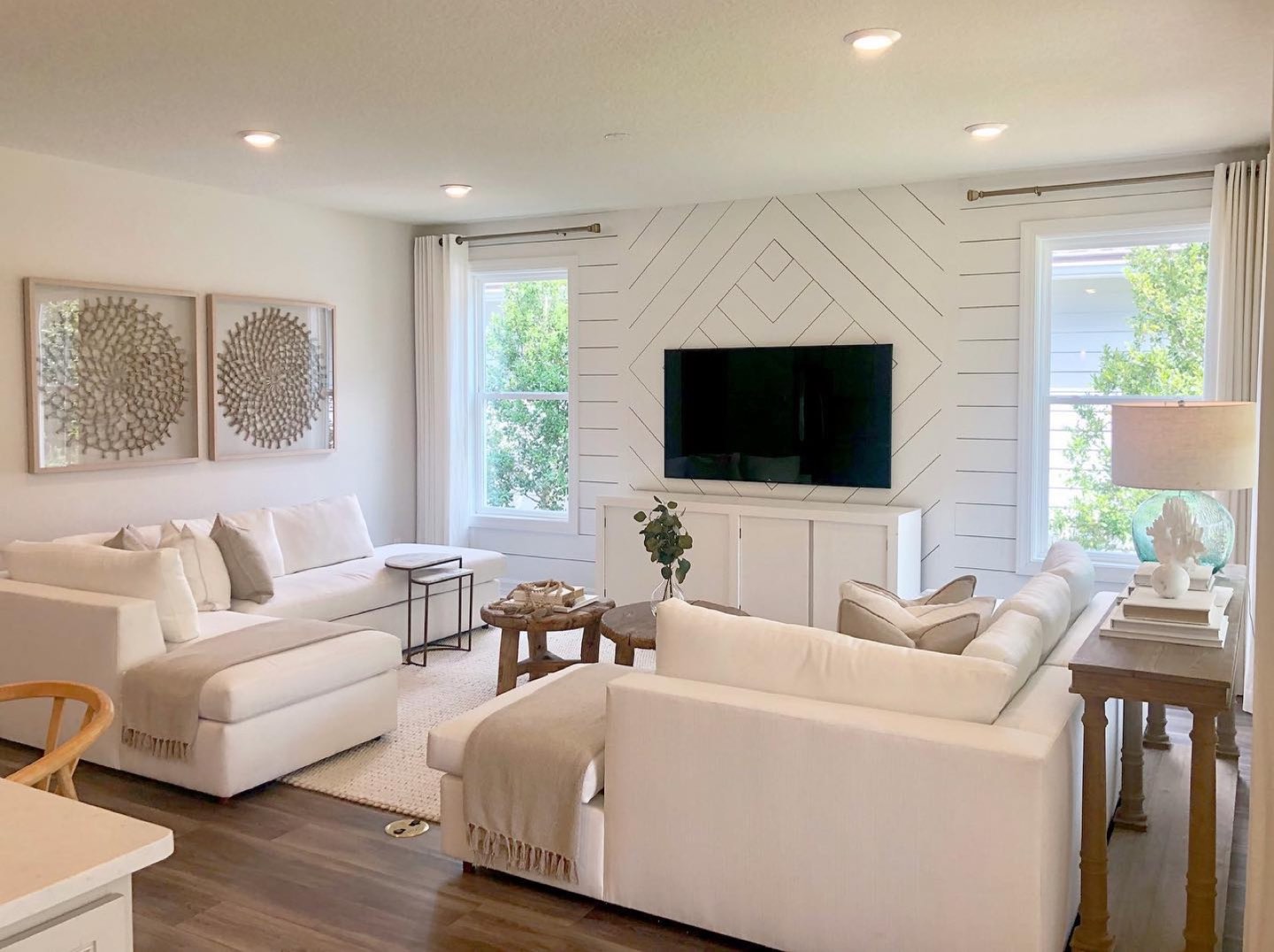 Bright living room with a diamond-pattern shiplap feature wall, white sectional sofas and a woven rug